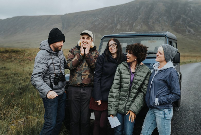 Group of friends standing in front of a car in the countryside.